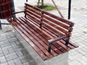 Banco de madeira sob base de concreto, com encosto e apoio de braço